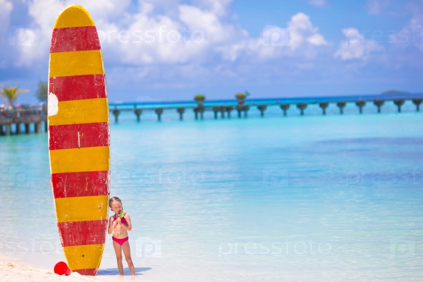 Adorable little girl with big surfboard during tropical vacation