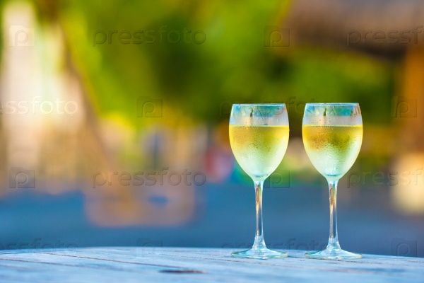 Two glasses of tasty white wine at sunset on wooden table