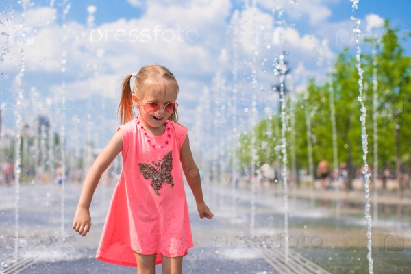 Little girl playing in open street fountain at hot sunny day