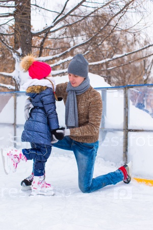 Young father and adorable little girl on skating rink outdoor