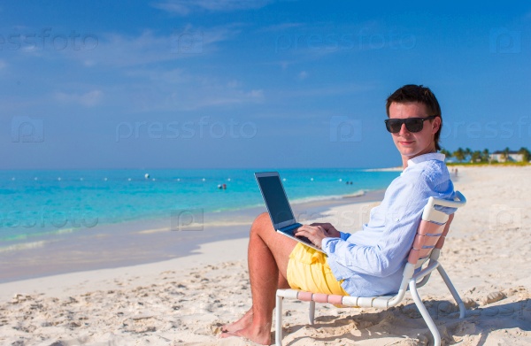 Young man with laptop and cell phone on tropical beach, stock photo