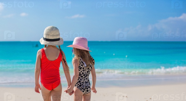 Back view of two little girls looking at the sea on white beach
