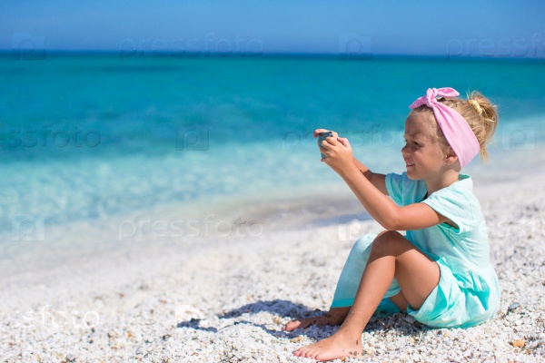 Little cute girl taking pictures on the phone at tropical beach
