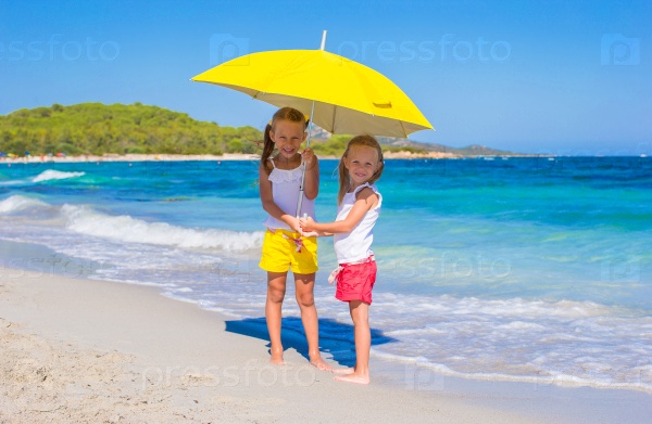 Little girls with big yellow umbrella walking on tropical beach