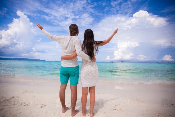Back view of young couple spread their arms standing on white sandy beach, stock photo