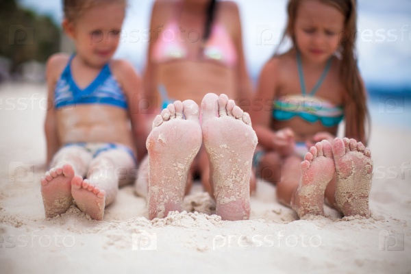 Closeup of the feet of mother and two daughters on the white sandy beach