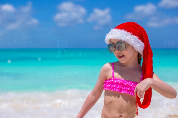 Little cute girl in red Santa hat on tropical beach