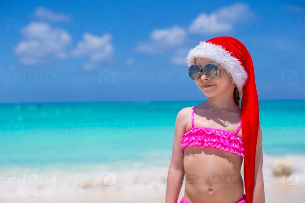 Little cute girl in red hat santa claus on the beach