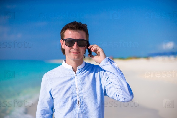 Young man with laptop and phone on the background of turquoise ocean at tropical beach, stock photo