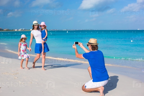 Young father making photo on phone of family at beach