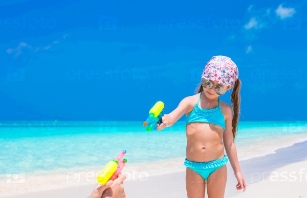 Little girl play with water pistol on tropical beach