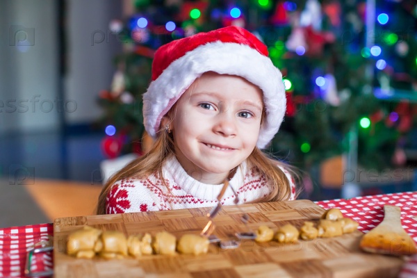 Adorable little girl with rolling pin baking gingerbread cookies for Christmas, stock photo