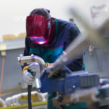 Industrial worker with protective mask welding inox elements in steel structures manufacture workshop, stock photo
