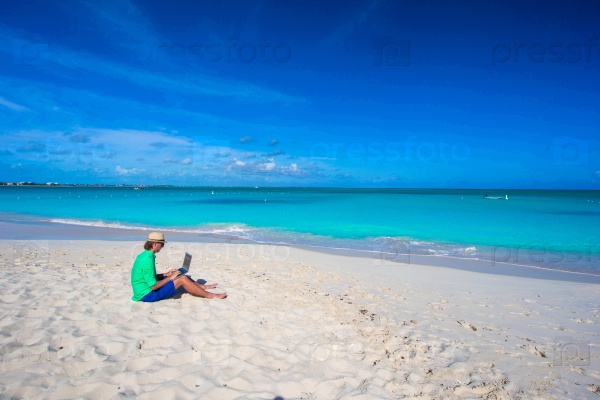 Young man using laptop on tropical beach