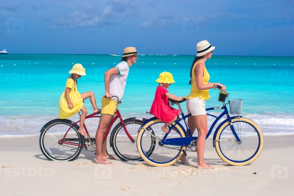 Young parents and kids riding bicycles on a tropical white sand beach