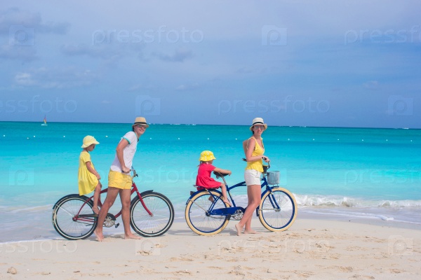 Young parents and little girls with bikes on a tropical white sandy beach