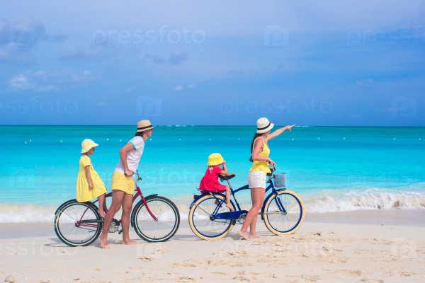 Young family with little kids ride bikes on a tropical exotic beach