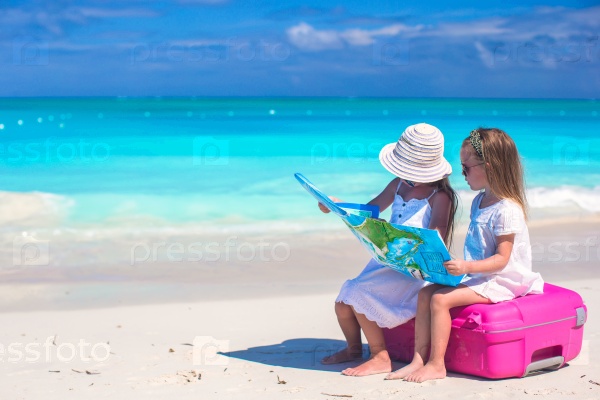 Little cute girls with big suitcase and a map on tropical beach, stock photo