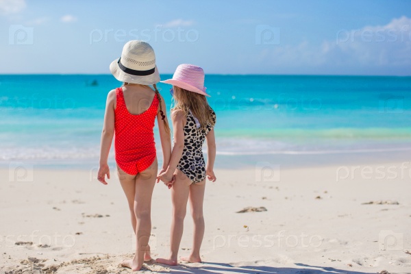 Back view of two little girls looking at the sea on white beach