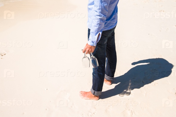 Closeup of two wineglasses in a man\'s hand on the white sandy beach, stock photo