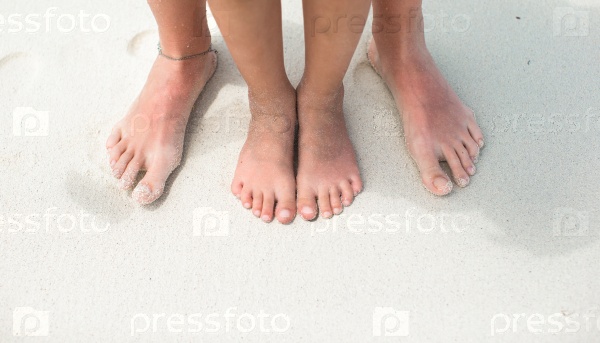 Closeup feet of a mom and kid on white sand beach