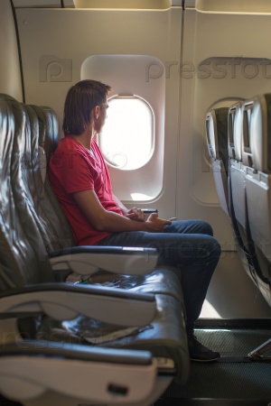 Young man looking in window on board of an airplane during the flight