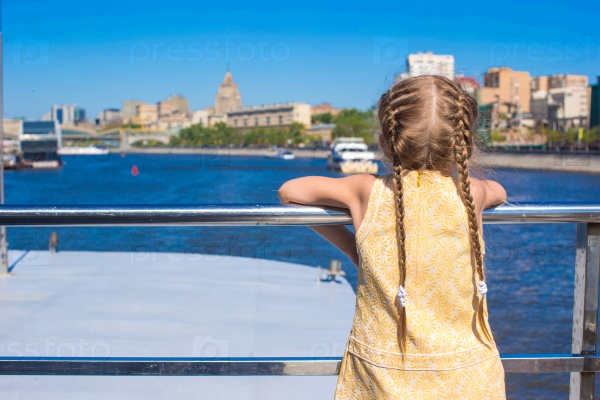 Little adorable girl on the deck of a ship sailing in big city