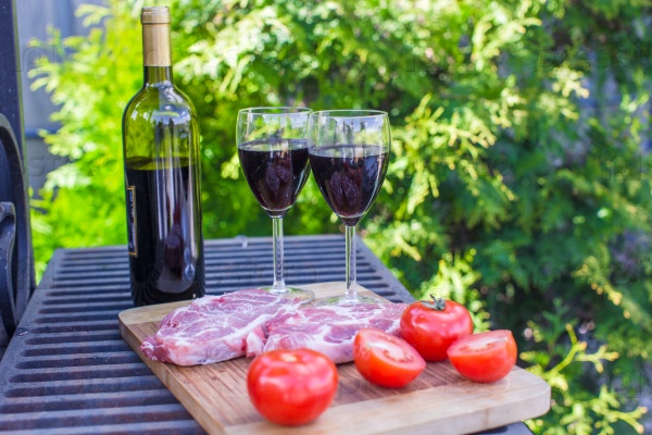 Bottle of red wine, steak and tomatoes on barbecue outdoors