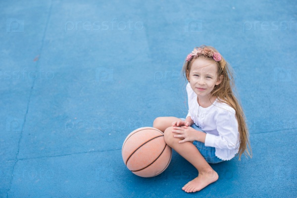 Little girl with basketball on the outdoor court at tropical resort