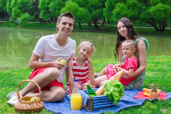 Happy young family picnicking outdoors near the lake