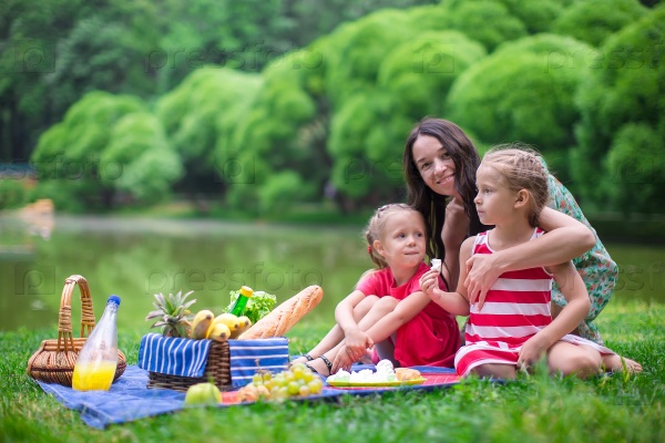Adorable little girls and happy mother picnicking in the park