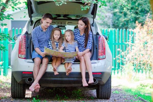 Family with two kids looking at map while traveling by car