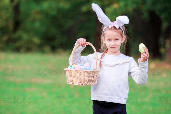 Adorable little girl wearing bunny ears holding a basket with Easter eggs on spring day, stock photo
