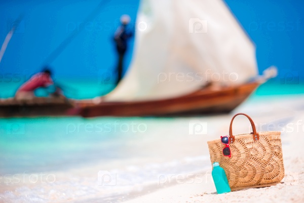 Beach accessories - straw bag, sunscreen bottle and red sunglasses on the beach, stock photo