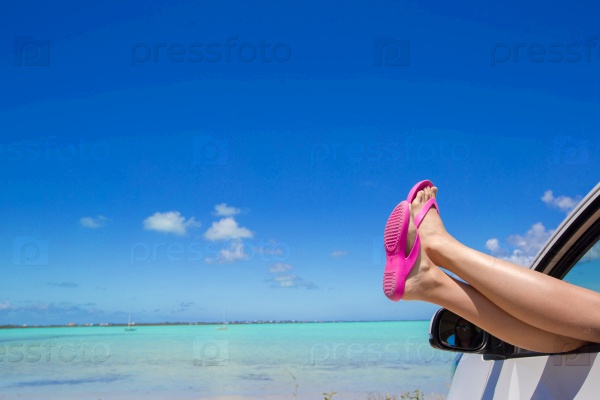 Close up pink flip flops from a car background of tropical beach and blue sky