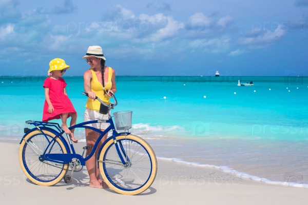 Happy mother and her daughter riding bicycles on a tropical beach