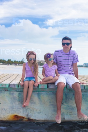 Family of three sitting on wooden dock enjoying ocean view