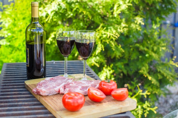 Two glass of red wine, steak and tomatoes on barbecue outdoors