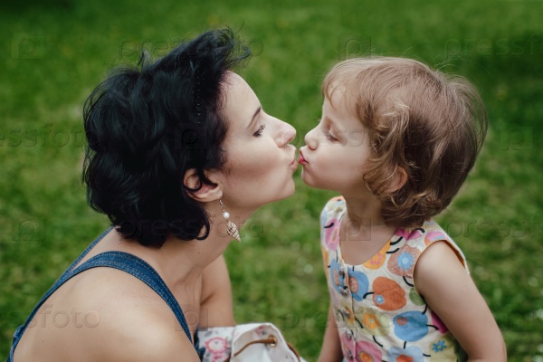 Mum kisses the daughter close-up on a background of grass, stock photo