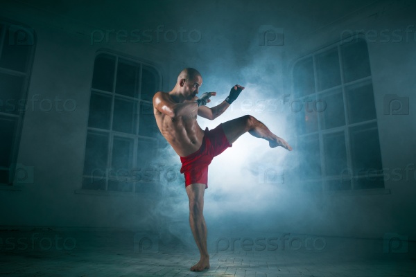 The young male athlete kickboxing on a background of blue smoke, stock photo