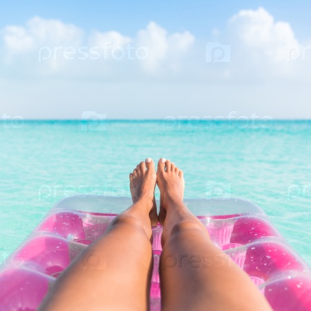 Summer vacation girl lower body closeup. Woman tanning legs  relaxing in ocean on pink inflatable swimming pool air mattress bed floating in turquoise water background. Suntan at tropical beach.