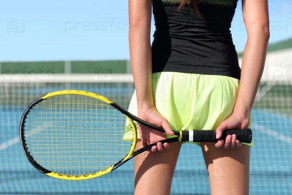 Tennis player holding racket preparing for playing game on outdoor court during summer. Closeup of hands and sport skirt with net in the background. Unrecognizable lower body of person from the back.