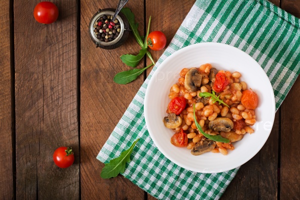 Stewed white beans with mushrooms and tomatoes with spicy sauce in a white bowl. Top view, stock photo