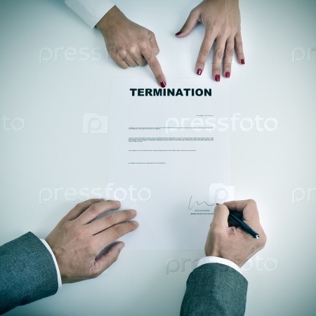 high-angle shot of the hands of a man who is signing a termination document on a desk in front of a young woman who is pointing the document