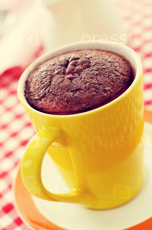 closeup of a chocolate mug cake in a yellow porcelain mug on a set table covered with a checkered tablecloth