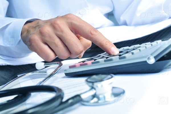 closeup of a young caucasian healthcare professional wearing a white coat calculates on an electronic calculator