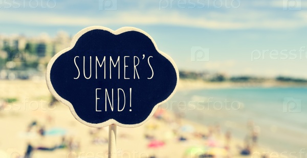 closeup of a chalkboard in the shape of a thought bubble with the text summers end written in it, with a blurred beach in the background, filtered