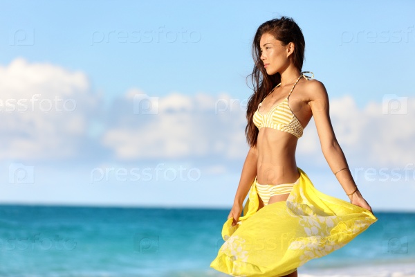 Sexy Asian woman with a slim stomach bikini body relaxing in sunset with yellow pareo cover-up swimwear and beachwear enjoying her weight loss on beach summer vacation in the Caribbean.