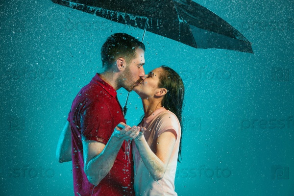 The loving couple in the rain with umbrella on a turquoise background, stock photo