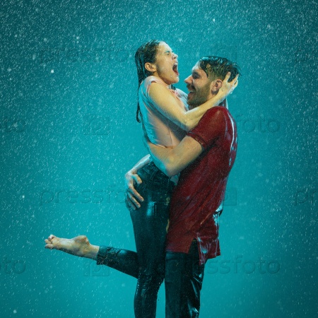 The loving couple kissing in the rain on a turquoise background, stock photo